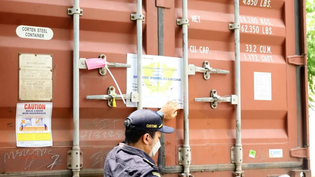 A Layered Container Security Strategy A shipping container door secured with multiple devices: a bolt seal, a heavy-duty barrier lock, and a GPS tracking unit.
