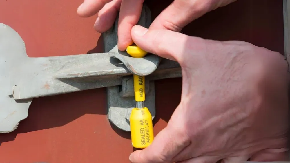 A hand applying a high-security bolt seal to a shipping container, representing the start of the sealing process.