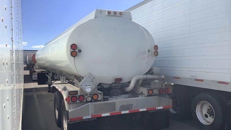 A large stainless steel tanker truck on a highway, with a focus on its valves and hatches.