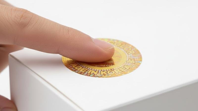 A close-up of a finger pressing down firmly on the edge of a newly applied hologram sticker for a final check.