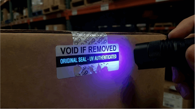 A hand holding a UV flashlight over a label, revealing a glowing blue text that was previously invisible.